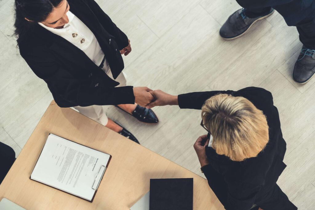 Two professionals shaking hands in a modern office setting, seen from above, symbolizing networking, trust, and professional connection—an image that fits an article about crafting a personal brand statement for career growth.
